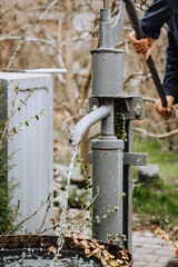 A man, a gardener pumps a hand pump from a metal well in the village, extracting water.