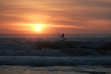 silhouette of a surfer jumping with a surfboard during sunset