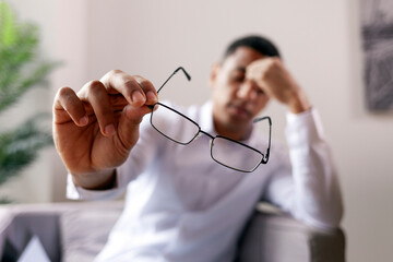 headache, african-american man takes off and holds glasses and wipes his closed eyes, office worker guy has sore eye