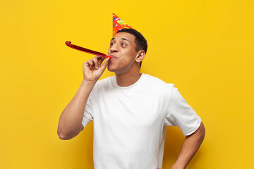 african american guy in festive hat celebrates his birthday and rejoices on yellow isolated...