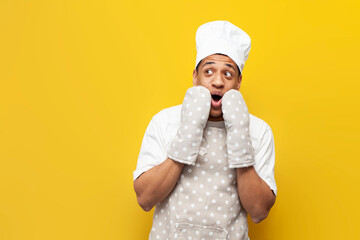 shocked guy african american baker in apron and gloves is surprised and looks at copy space on...