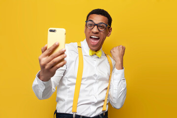 young african american guy in white shirt with suspenders and bow tie uses smartphone and rejoices...