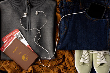 Close up of gray jumper, jeans, beige shoes, passport, tickets, smartphone and earphones