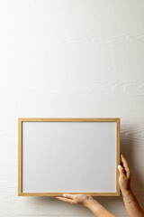 Vertical of hands holding empty wooden frame with copy space against white wall