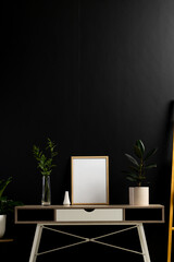 Vertical of hands holding empty wooden frame with copy space and plants on desk against black wall