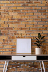 Vertical of empty wooden frame with copy space and plant in pot on desk against brick wall