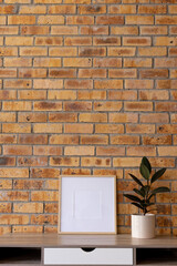 Vertical of empty wooden frame with copy space and plant in pot on desk against brick wall