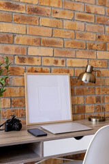 Vertical of empty wooden frame with copy space, plants and technology on desk against brick wall