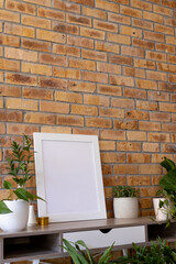 Vertical of empty white frame with copy space and plants in pots on desk against brick wall
