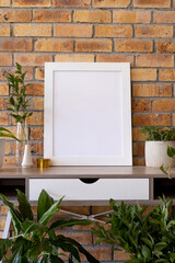 Vertical of empty white wooden frame with copy space and plants in pots on desk against brick wall