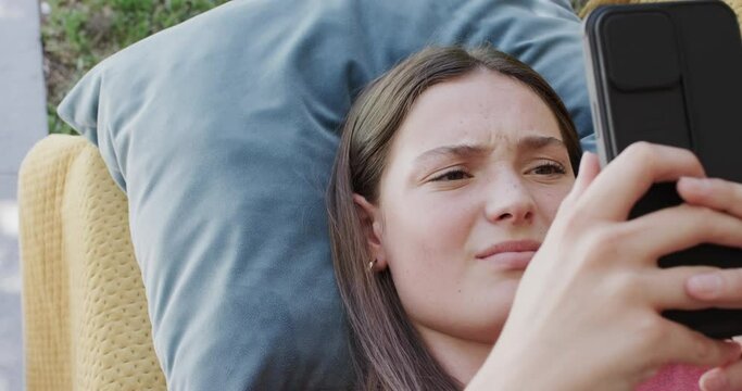 Thoughtful, upset caucasian teenage girl texting on smartphone and lying in slow motion