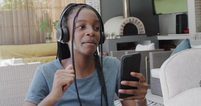 Happy african american teenage girl with headphones listening to music with smartphone