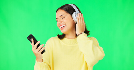 Happy woman, phone and dancing with headphones on green screen for audio track against a studio background. Female with headset listening to music on smartphone enjoying dance to sound on mockup