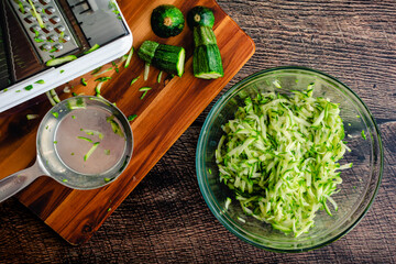 Shredded Zucchini in a Glass Mixing Bowl: Grated zucchini shown with a mandoline and other tools