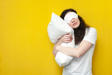 young girl in sleep mask and pajamas sleeps hugging pillow on yellow background, healthy sleep...