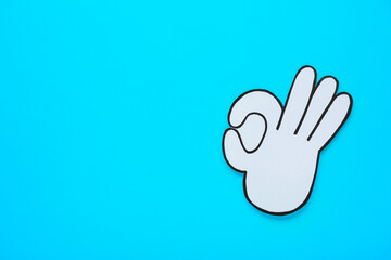 Paper cutout of okay hand gesture on light blue background, top view. Space for text