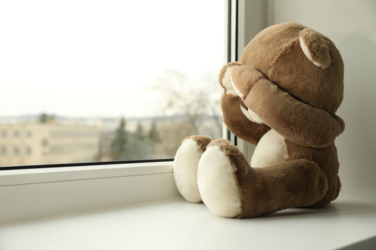 Cute lonely teddy bear on windowsill indoors. Space for text
