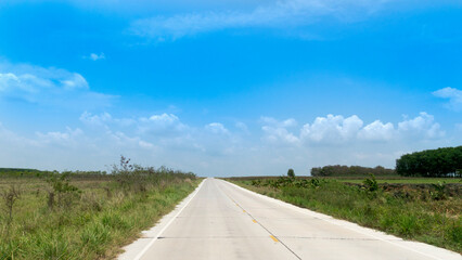 Country concrete road in Thailand. sunny road on the open space of the meadow two beside of road. under the blue sky and white clouds.
