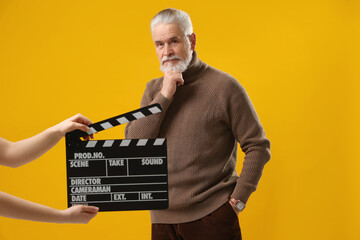 Senior actor performing while second assistant camera holding clapperboard on yellow background....