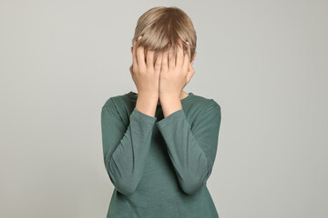 Boy covering face with hands on light grey background. Children's bullying