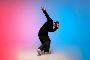 young guy dancer in black clothes break dancing in neon lighting, man performs hip hop movement in...