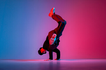 young guy dancer is dancing break in neon lighting, male acrobat is doing trick and dance exercise