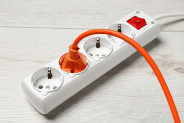 Power strip with extension cord on white wooden floor, closeup. Electrician's equipment