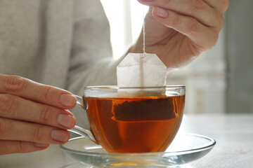Woman taking tea bag out of cup at table indoors, closeup