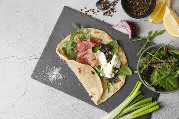 Delicious pita wrap with jamon, cheese cream and greens on light gray table, flat lay