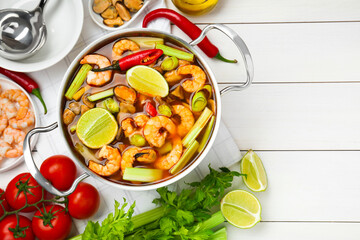 Saucepan with delicious Tom Yum soup and ingredients on white wooden table, flat lay. Space for text