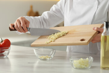 Professional chef putting cut garlic into bowl at white marble table indoors, closeup