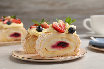 Pieces of tasty meringue roll with jam, cream, strawberry, blueberry and mint on light grey marble...