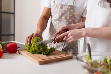 multiracial young couple preparing veggie vegetable and greens salad in white modern kitchen