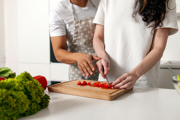 african american man helping and teaching woman how to cut tomatoes, young multiracial couple preparing salad