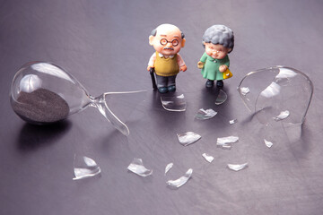 miniature people. a couple of elderly people near a broken hourglass. life time crisis. the concept...