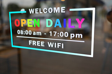 The storefront sign reads welcome to open daily and the rainbow lettering communicates support for LGBT or gender diversity.
