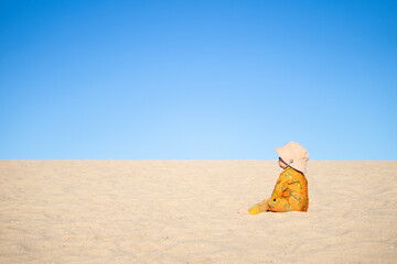 Baby sitting on sand dune contemplating life looking at bright blue sky