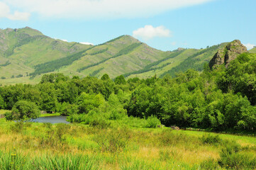 A fragment of a small picturesque lake at the edge of a forest surrounded by high mountains.