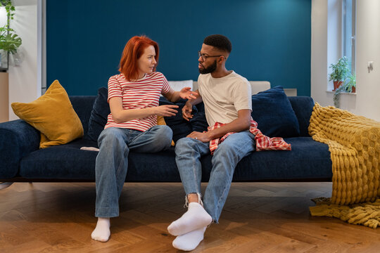 Interracial relationships problems. Unhappy young diverse married couple talking about problems in relationship, having misunderstandings, sit on sofa in living room. Hardships in marriage