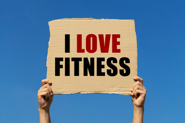 I love fitness text on box paper held by 2 hands with isolated blue sky background. This message board can be used as business concept about fitness.