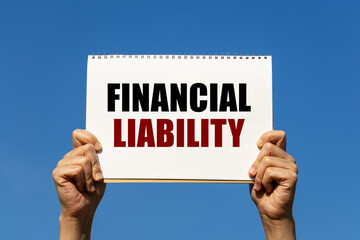 Financial liability text on notebook paper held by 2 hands with isolated blue sky background. This message can be used as business concept about financial liability.