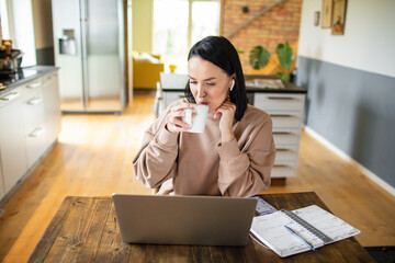 Young adult woman working on her laptop in the kitchen of her home