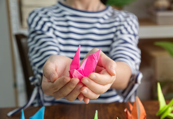 close-up photo of Two hands holding a bird folded from pink origami paper. tenderly And there were...