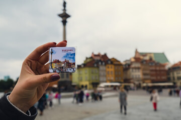 Female woman traveler holding magnet from vacation holiday concept old town main square in Warsaw Poland. City landmarks. Tourist attraction 