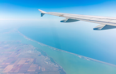Obraz premium View from the airplane window at a beautiful blue clear sky, earth, sea and the airplane wing