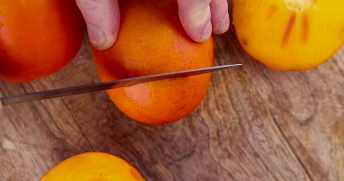 Half-ripe orange persimmon, fresh ripe persimmon cut into pieces on a cutting board with a sharp knife