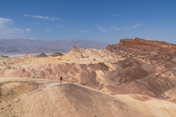 Fototapeta na wymiar Man with scenic view of summit peak Manly Beacon seen from Zabriskie Point, Badlands, Furnace creek, Death Valley National Park, California, USA. Erosional landscape of Amargosa Chaos rock formation