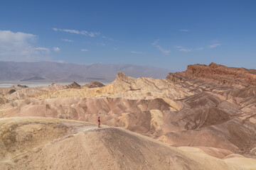 Fototapeta na wymiar Man with scenic view of summit peak Manly Beacon seen from Zabriskie Point, Badlands, Furnace creek, Death Valley National Park, California, USA. Erosional landscape of Amargosa Chaos rock formation