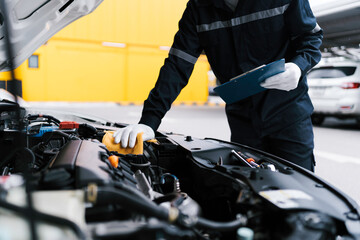 Automobile mechanic repairman checking a car engine by inspecting and writing to the clipboard the...