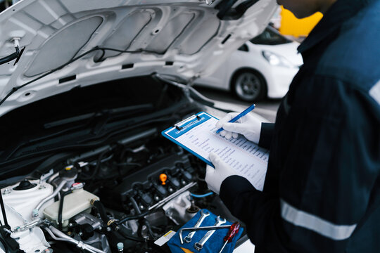 Automobile mechanic repairman checking a car engine by inspecting and writing to the clipboard the checklist for repair machine and car service for maintenance and maintenance check concept.